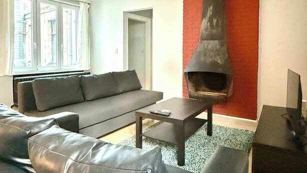 A modern living room with a black leather sofa, a coffee table, and a fireplace.