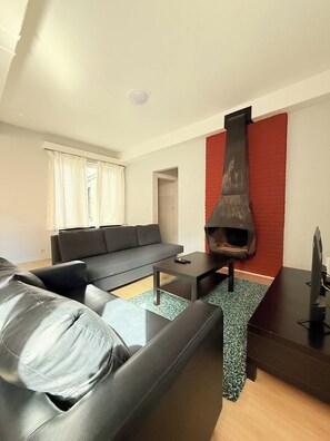A modern living room with a black sofa, a coffee table, a fireplace, and a TV stand. - Stay in the Heart of Brussels – Steps from Grand Place & Manneken Pis (Brussels)