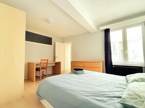 A bedroom with a bed, a desk, and a chair.