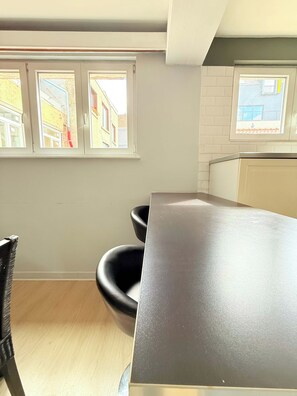 A kitchen with a dark countertop, two black chairs, and a window with a view of buildings.