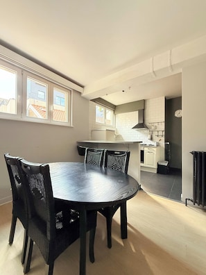 A dining area with a round table and chairs, a kitchen in the background, and a view through the window. - Stay in the Heart of Brussels – Steps from Grand Place & Manneken Pis (Brussels)