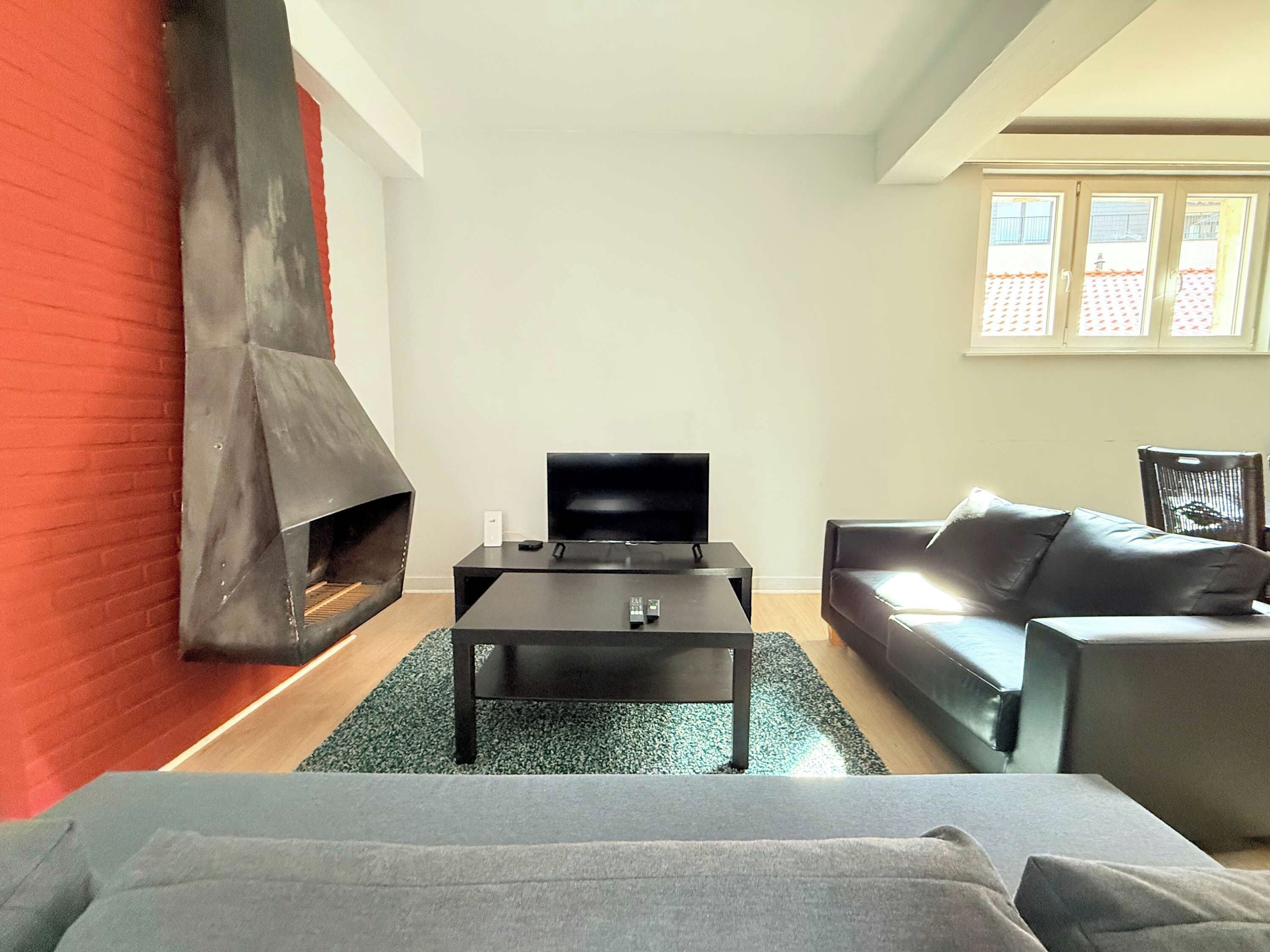 Un salon moderne avec une cheminée, un téléviseur posé sur une table noire et un canapé gris.