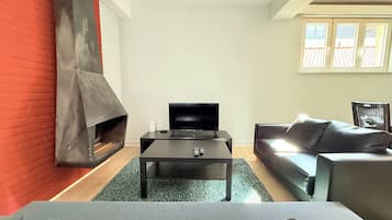 Un salon moderne avec une cheminée, un téléviseur posé sur une table noire et un canapé gris.