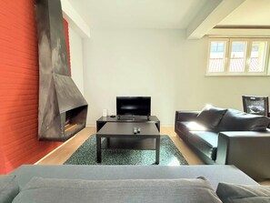 A modern living room with a fireplace, a television on a black table, and a grey sofa.