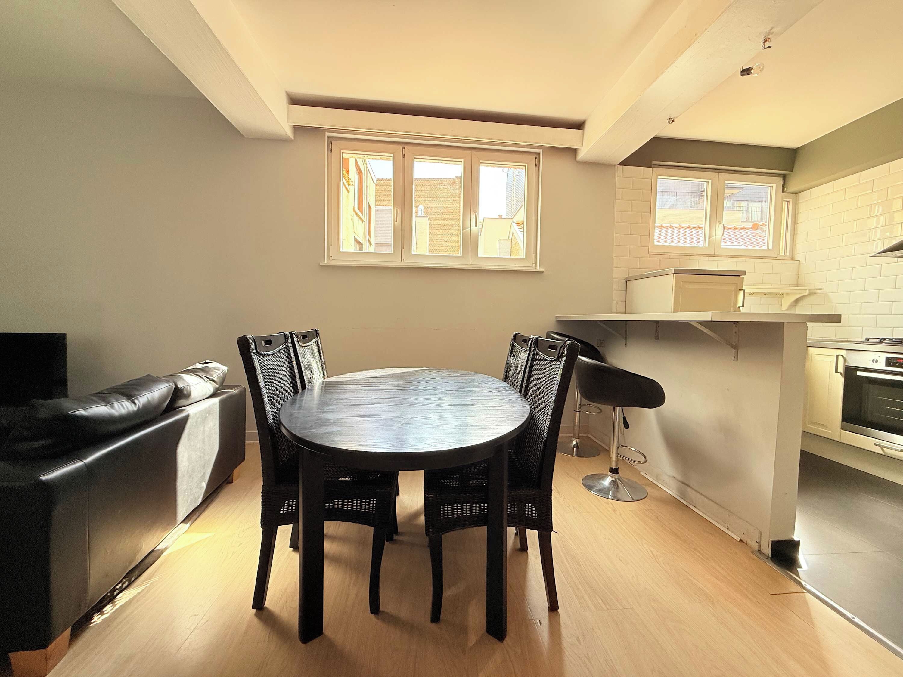 A dining area with a round table and chairs, a kitchen with white cabinets, and a window with a view of the outside.
