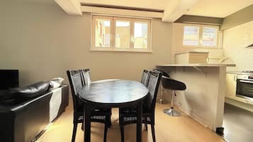 Een eetgedeelte met een ronde tafel en stoelen, een keuken met witte kasten, en een raam met uitzicht.