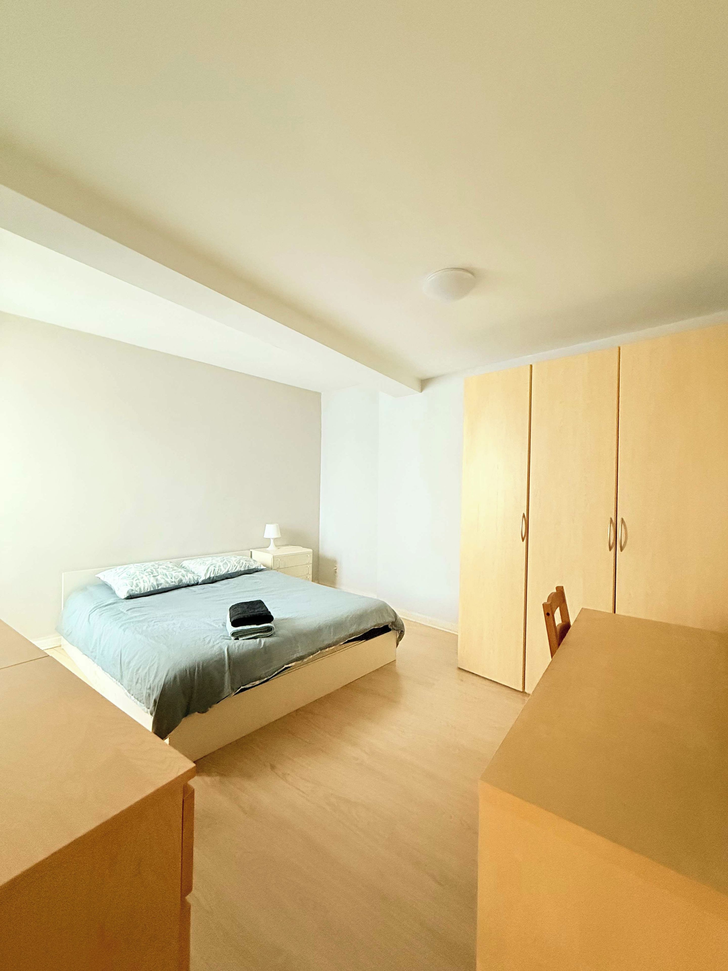 A bedroom with a bed, bedside table, lamp, wardrobe, and a table with chairs.