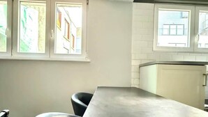 A modern kitchen with a central island, two black bar stools, and a view of buildings through the windows.