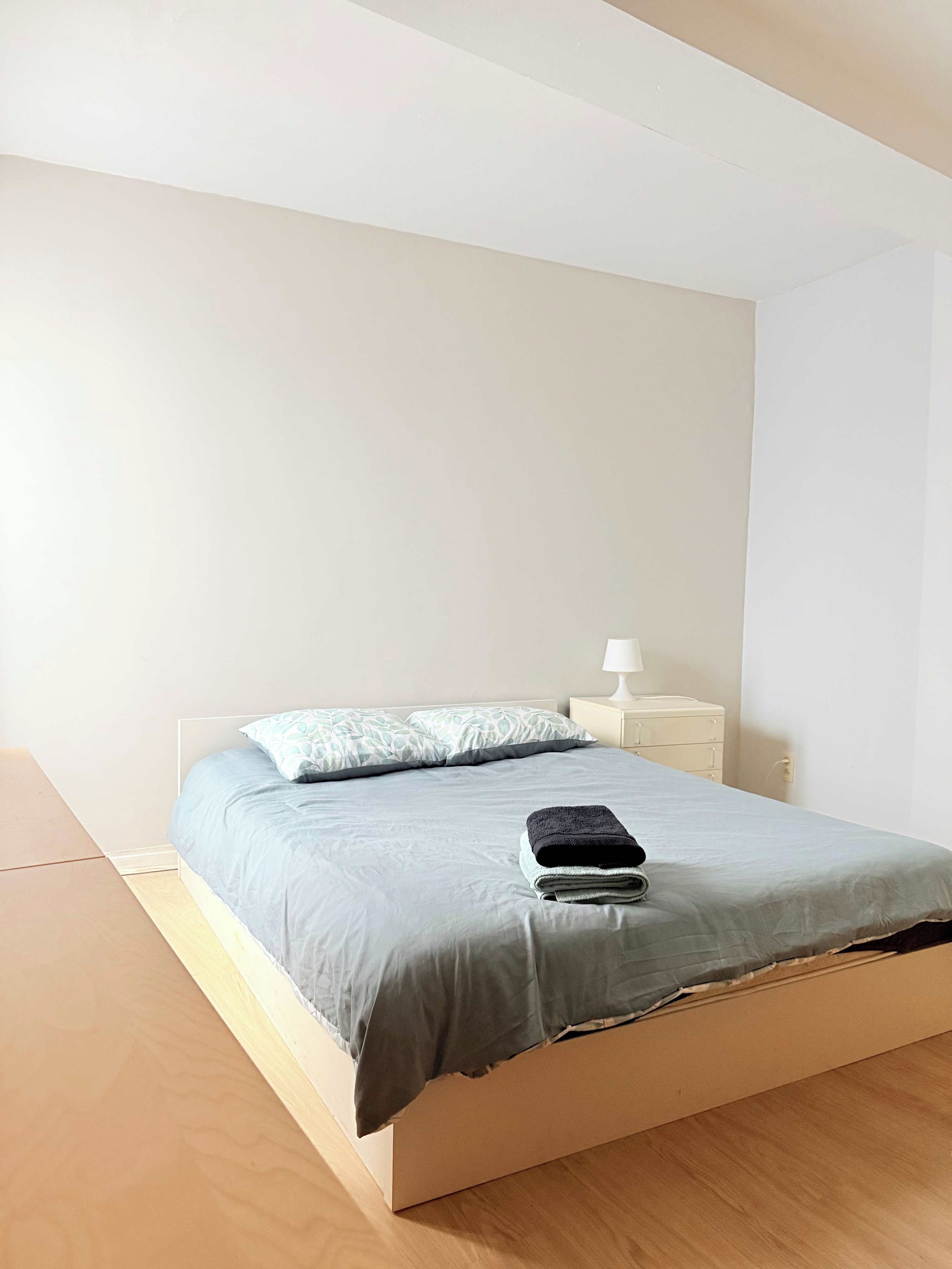 A minimalist bedroom with a single bed, a nightstand, and a lamp.