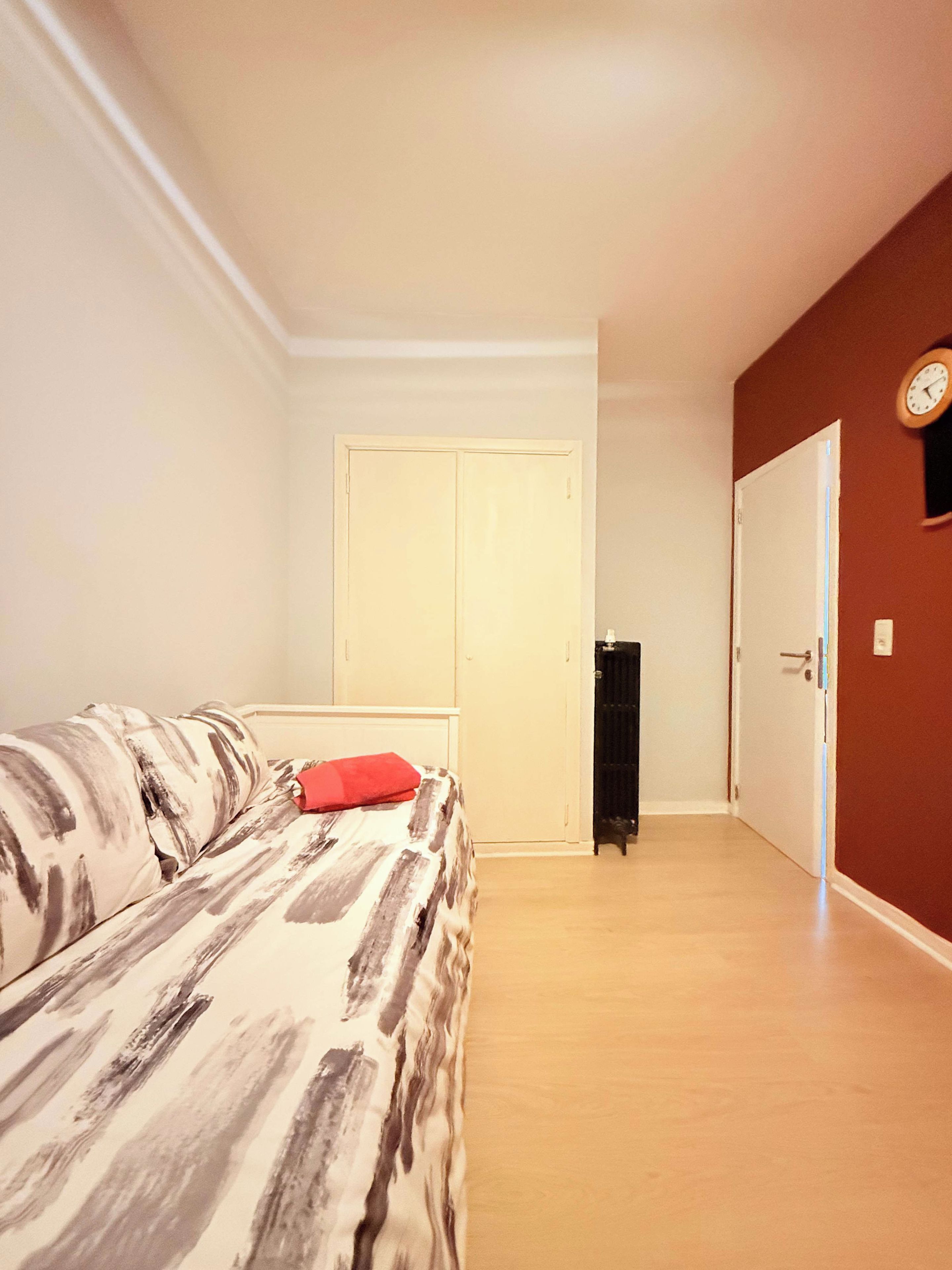 Een slaapkamer met een bed, een kledingkast, een radiator en een klok aan de muur.