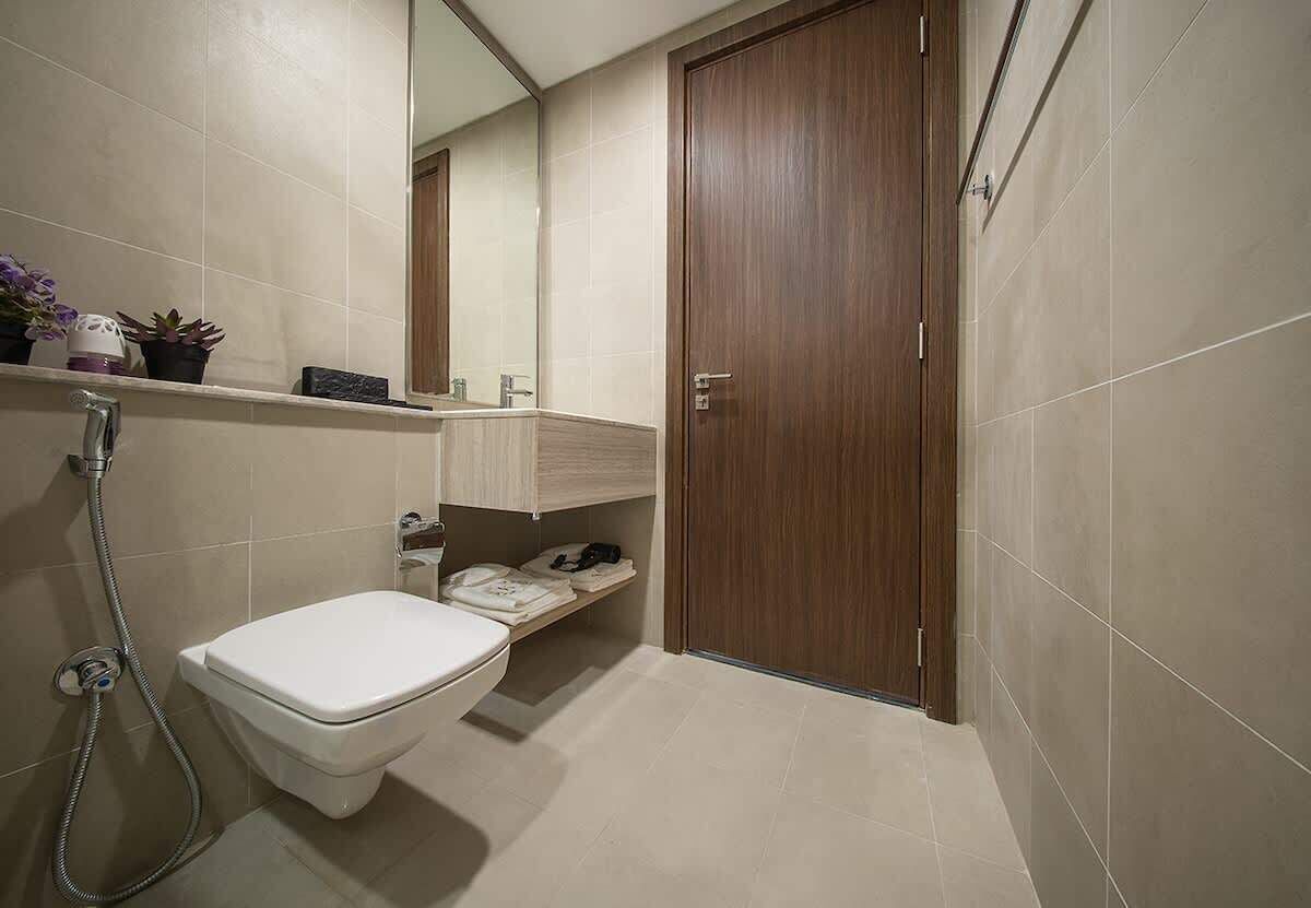 Un baño con inodoro, ducha, espejo, repisa con artículos de aseo y puerta de madera.