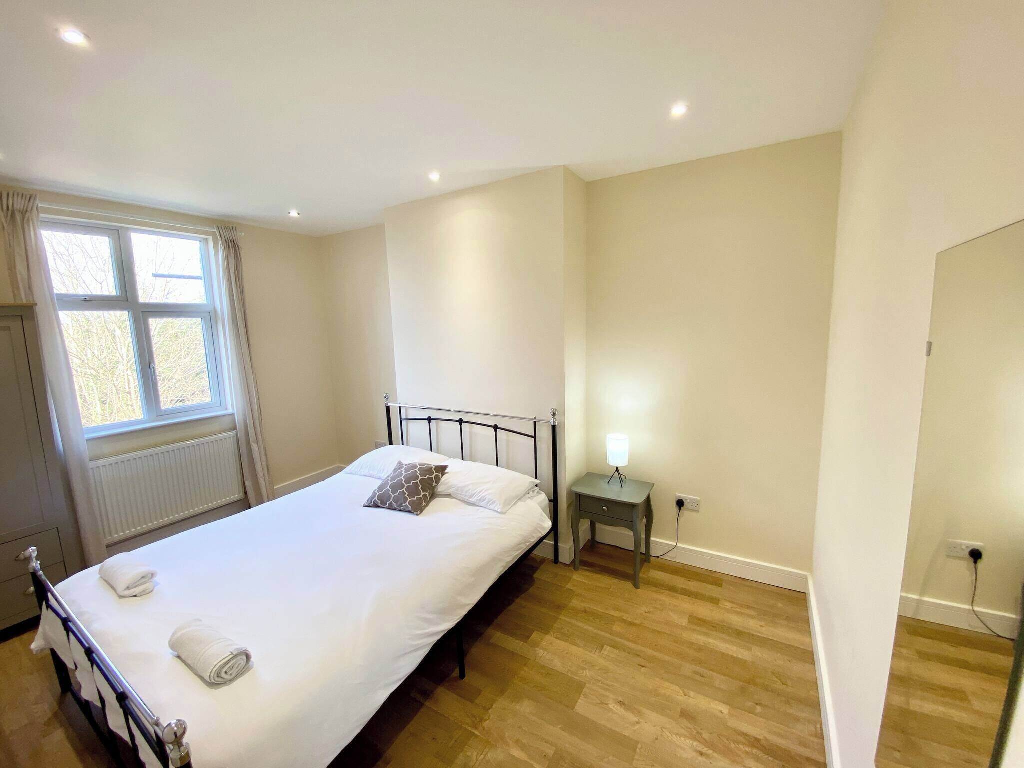 A bedroom with a single bed, a bedside table with a lamp, a window with curtains, and a radiator.