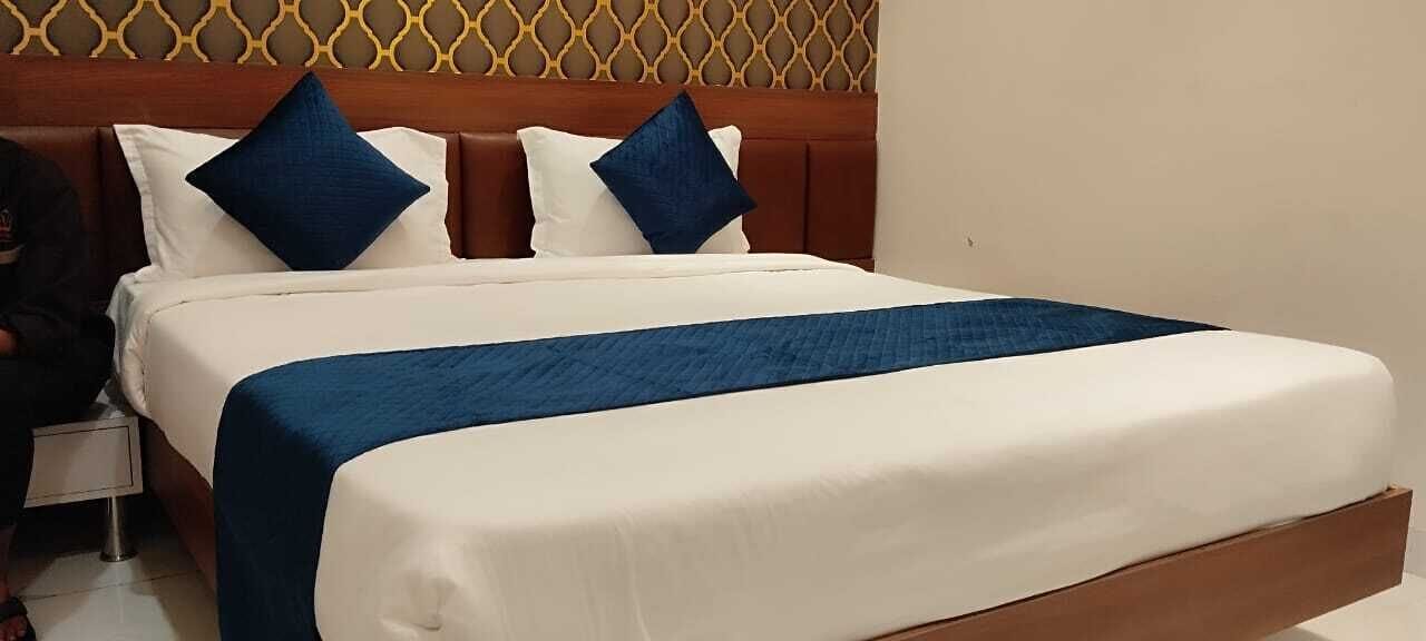 A neatly made bed with a white and blue bedspread and two blue pillows.