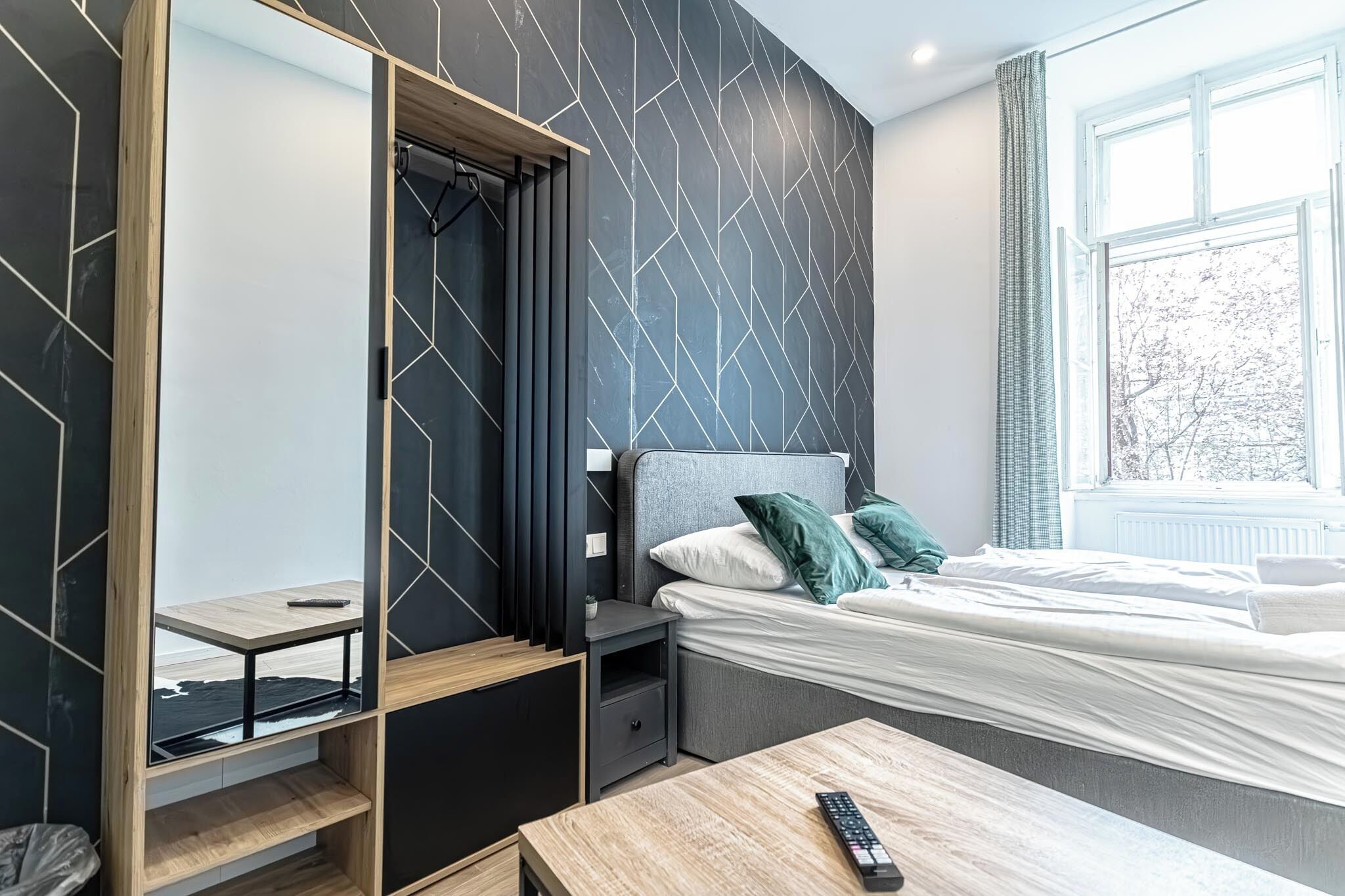 Moderni hotellihuone, jossa on sänky, yöpöytä, puinen pöytä ja peili.