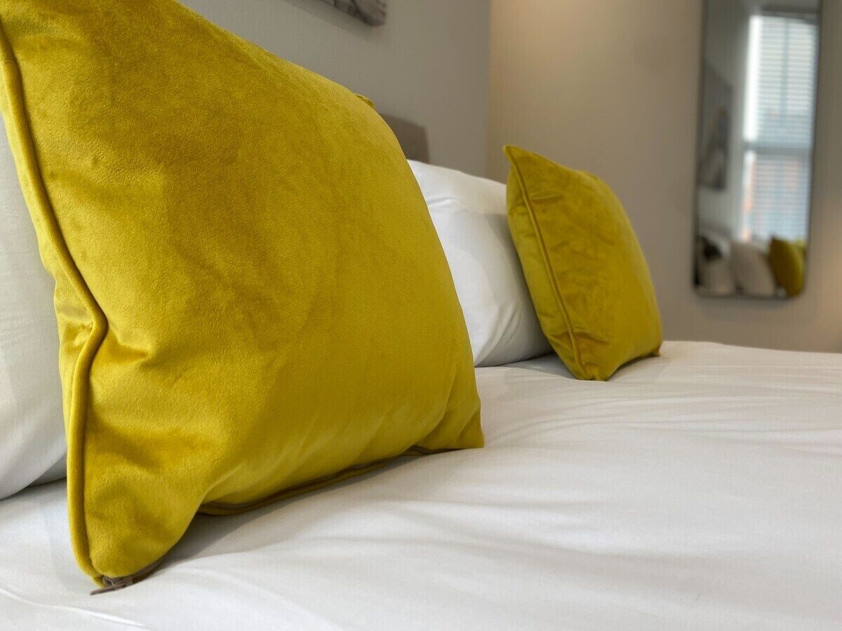 A bed with white bedding and two yellow pillows.