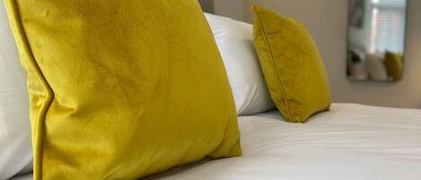 A bed with white bedding and two yellow pillows.