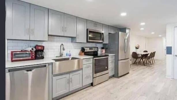 A modern kitchen with stainless steel appliances, grey cabinets, and a dining area with a table and chairs. - Charming townhome ground floor/basement unit (Washington)
