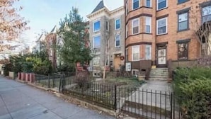 A row of multi-story residential buildings with a sidewalk and a black metal fence in front. - Charming townhome ground floor/basement unit (Washington)