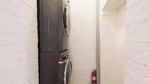 A laundry room with a washing machine and dryer, a fire extinguisher, and white brick walls. - Charming townhome ground floor/basement unit (Washington)
