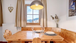 A wooden dining table with chairs, a hanging light fixture, a window with curtains, and a framed picture on the wall. - Apartment 'Panorama Val Di Non' with Mountain View, Wi-Fi, and Air Conditioning (Unsere Liebe Frau im Walde-St. Felix)