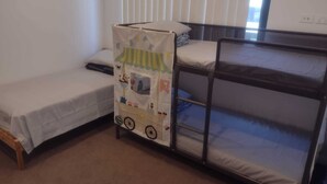 A room with a bunk bed, a single bed, and a small table with a colorful tablecloth.
