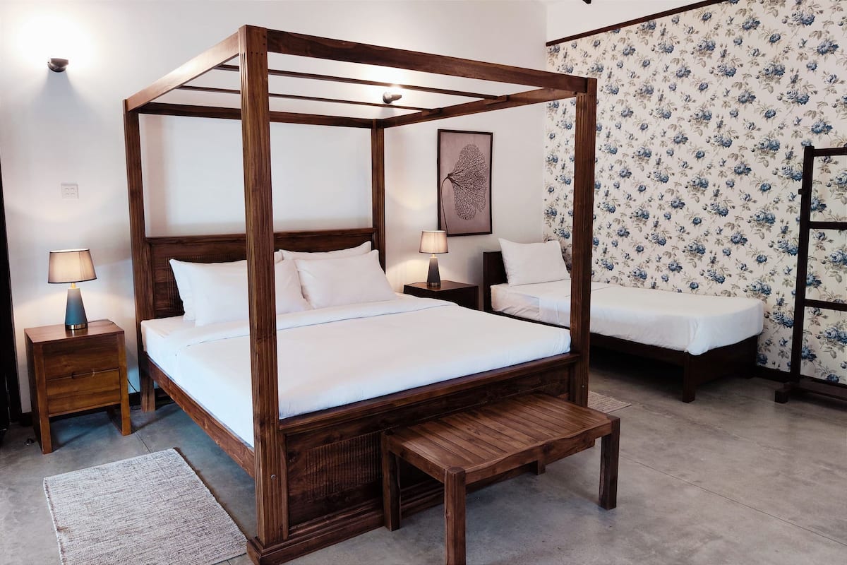 Ein Himmelbett mit Holzbettgestell, zwei Nachttische und eine Sitzbank.