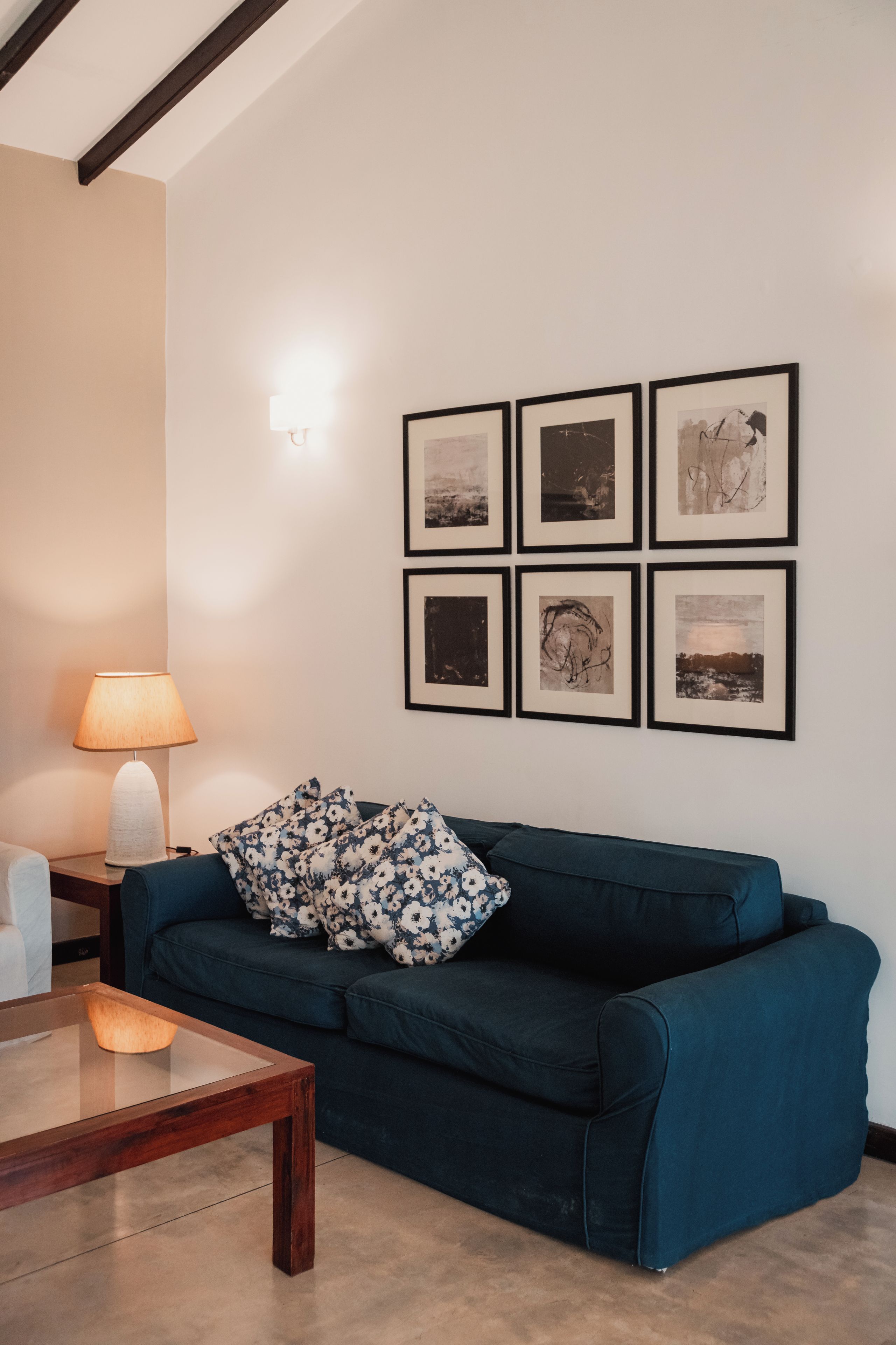 A living room with a dark blue sofa, a glass coffee table, a lamp, and six framed pictures on the wall.