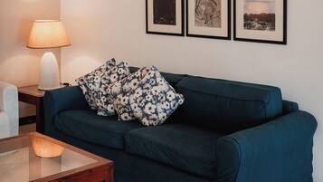 A living room with a dark blue sofa, a glass coffee table, a lamp, and six framed pictures on the wall.