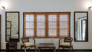 Une pièce avec deux chaises en bois, une petite table et une grande fenêtre avec des stores.