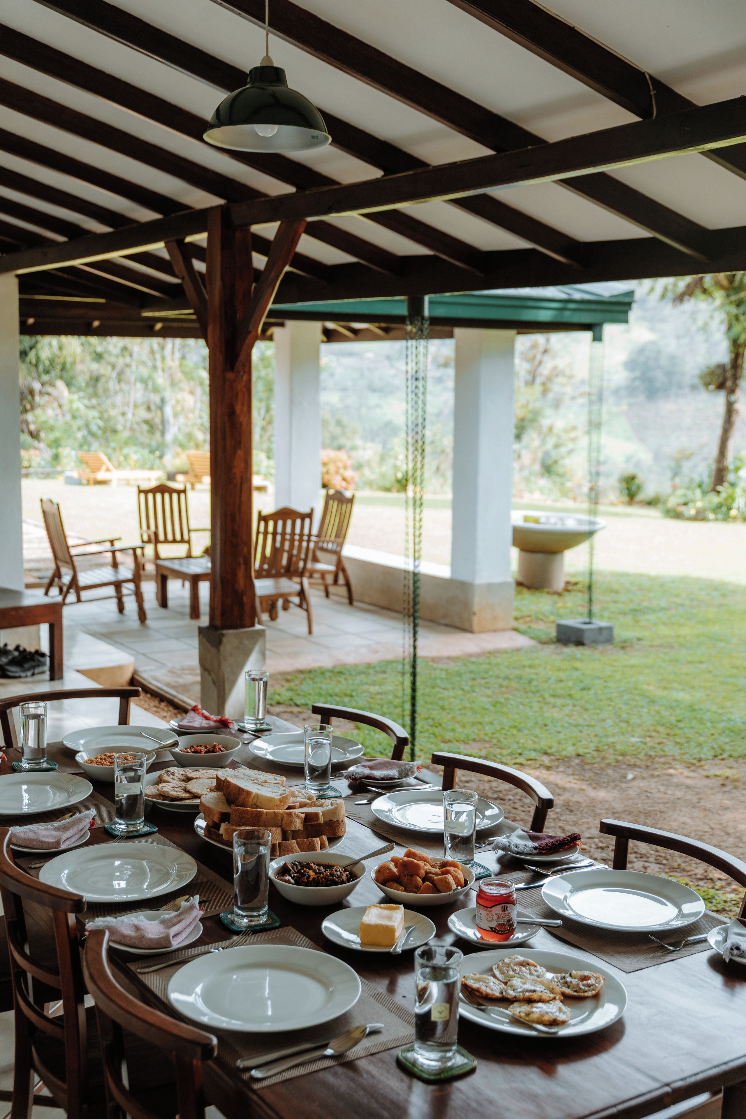An outdoor dining area with tables set for a meal, chairs, and a view of the garden.