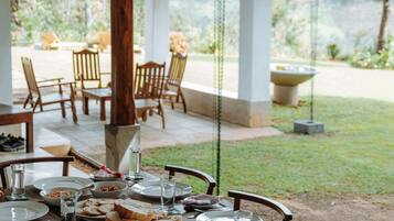 An outdoor dining area with tables set for a meal, chairs, and a view of the garden.