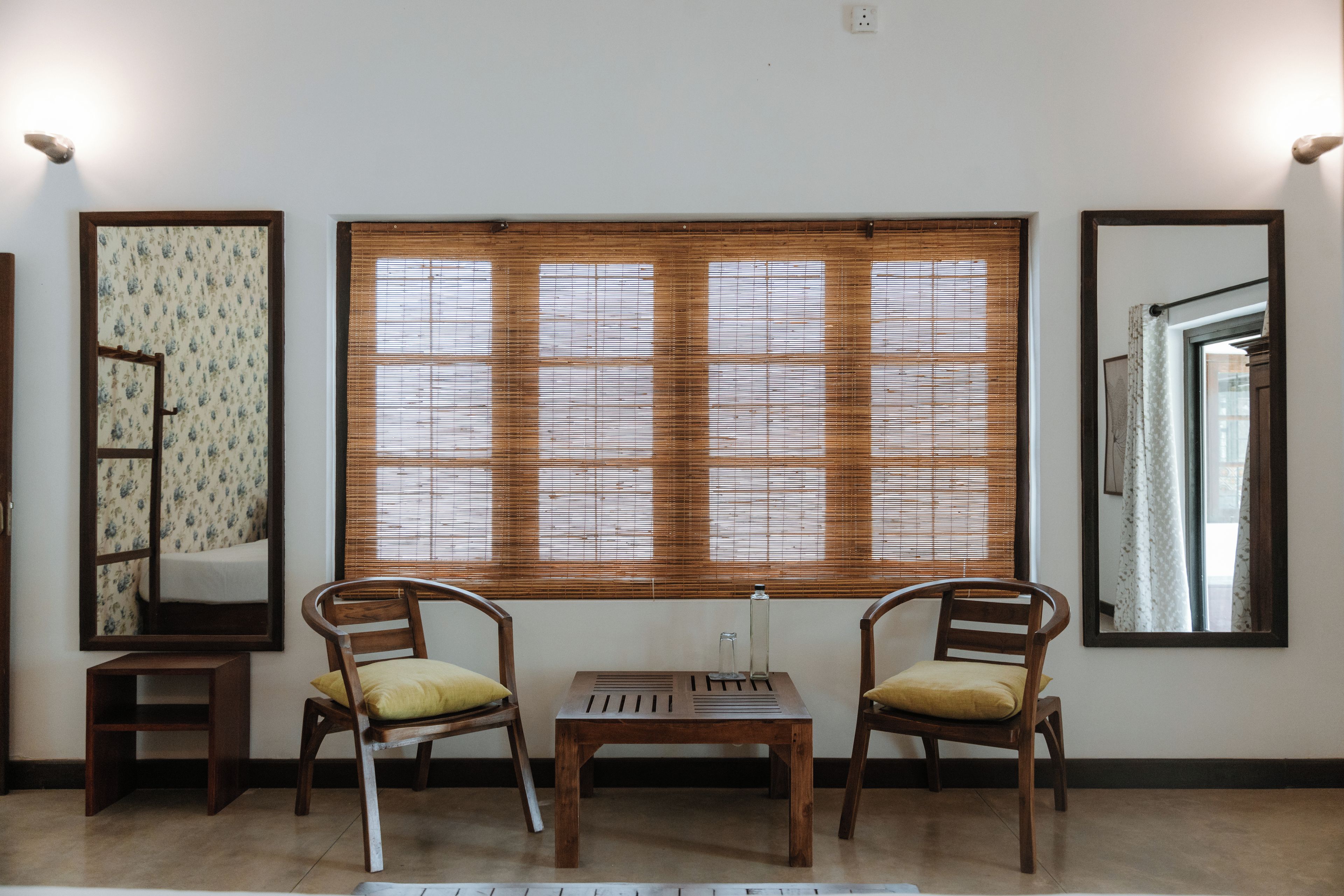 A room with two wooden chairs, a small table, and a large window with blinds.
