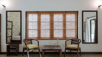 A room with two wooden chairs, a small table, and a large window with blinds.