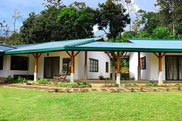 A two-story building with a green roof and white walls, featuring a covered porch with wooden pillars and a chair.
