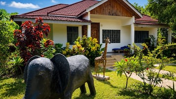 A house with a red-tiled roof, a front porch, and a garden with a giraffe and an elephant statue.
