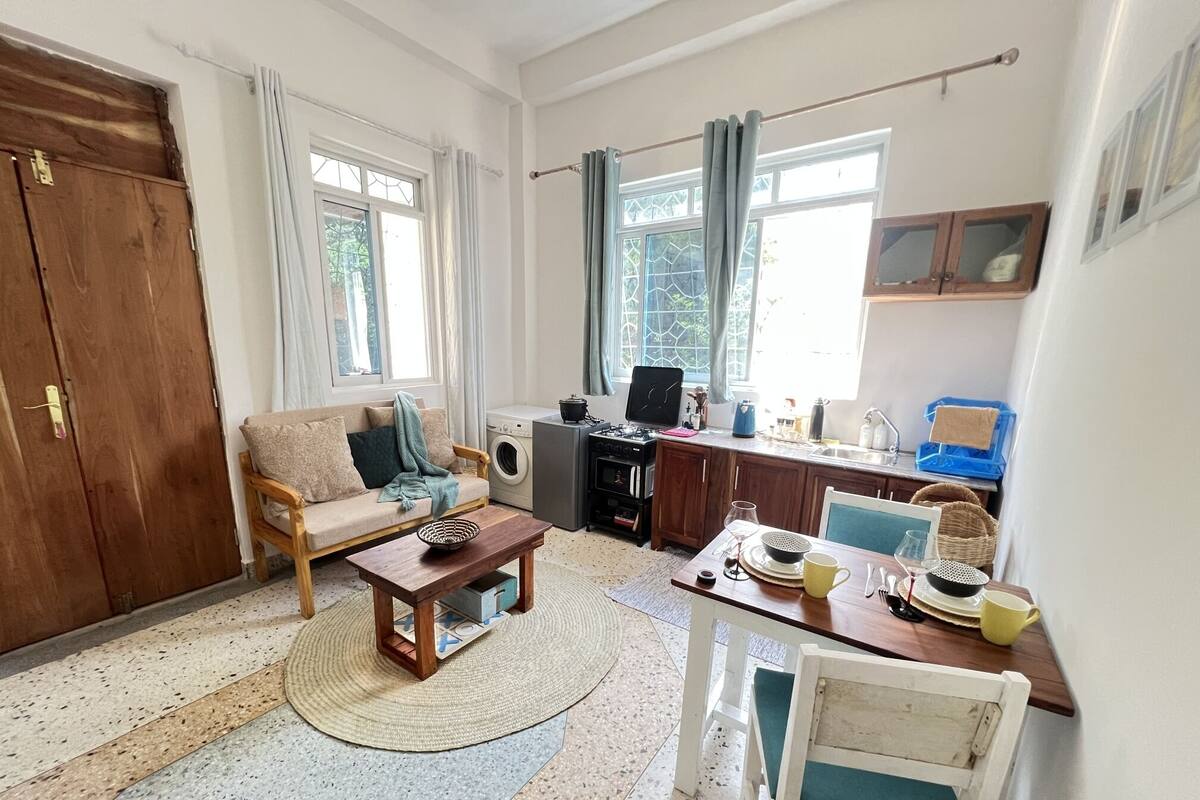 Una sala de estar acogedora con un sofá, una mesa de centro y un comedor con una silla y una mesa. Hay una lavadora y una estufa en la cocina.