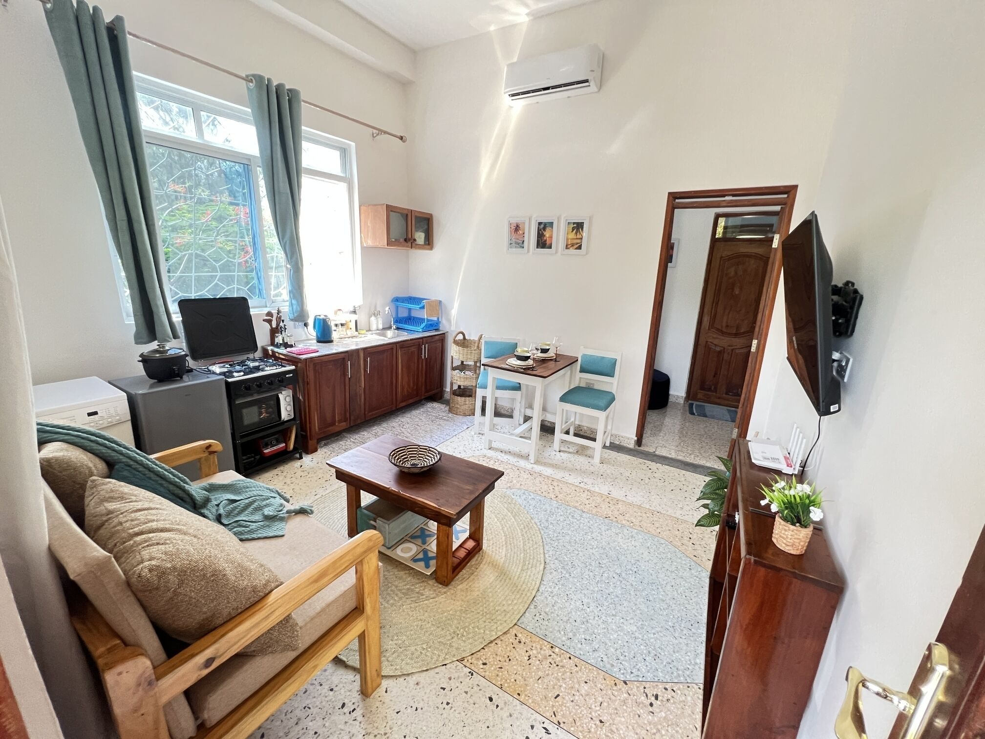 Un salón con sofá, una mesa de centro y televisor. Se observa una zona de cocina con armarios y una mesa de comedor con sillas.