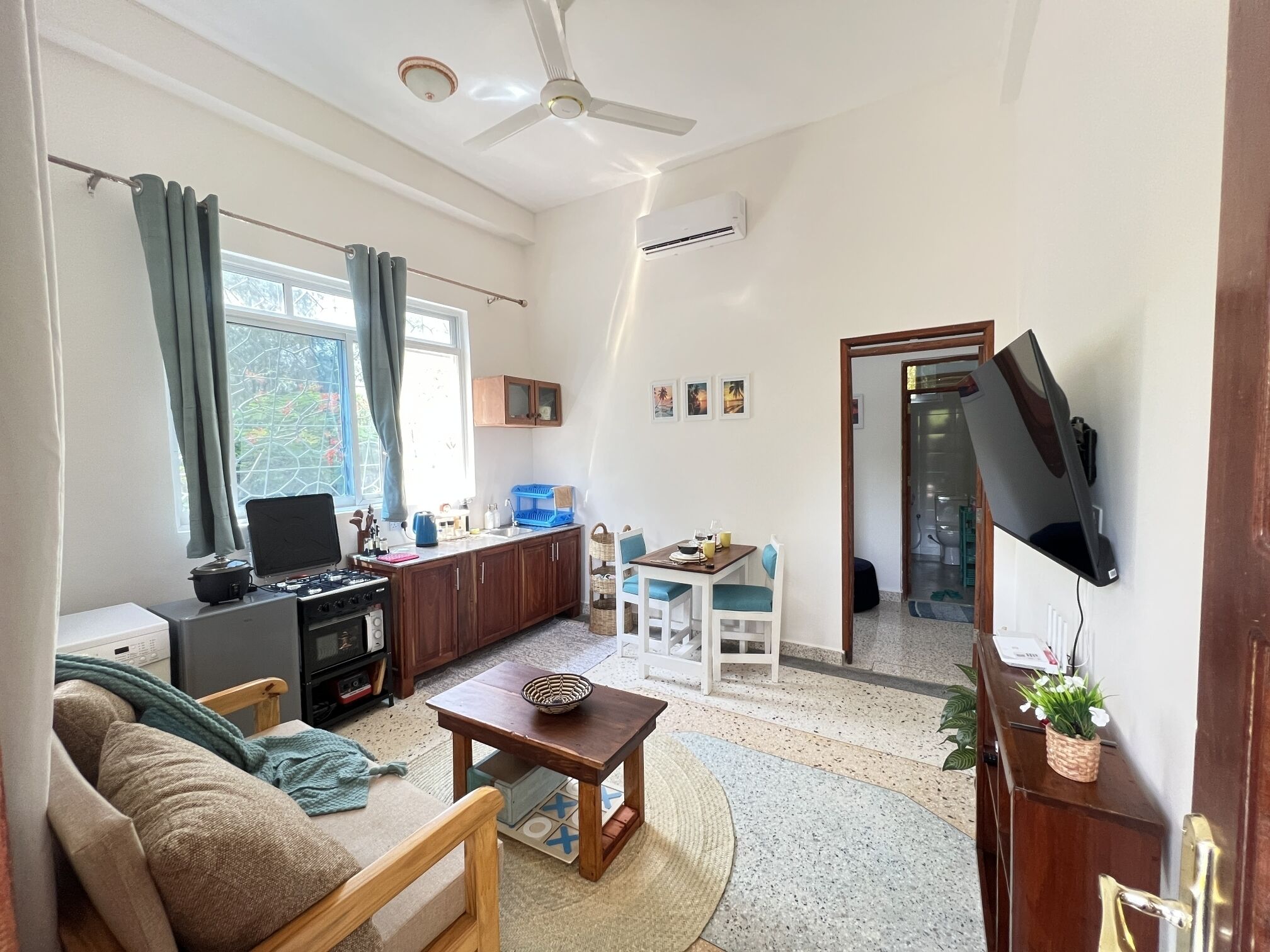 A compact living space with a kitchenette, a dining area, and a TV mounted on the wall.