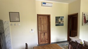 A dining area with a wooden table and chairs, a wooden door, a wall-mounted air conditioner, and a small picture on the wall. - Diamond Coast Villa and Apartments (Paje)