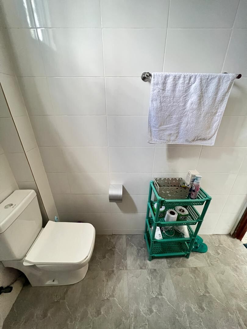 A bathroom with a white toilet, a green storage unit with toiletries, and a white towel hanging on a rack.