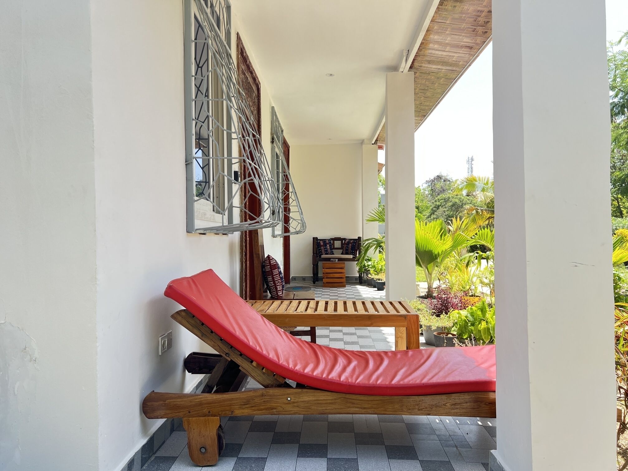 A sun lounger on a balcony with a view of a garden and a dining area.