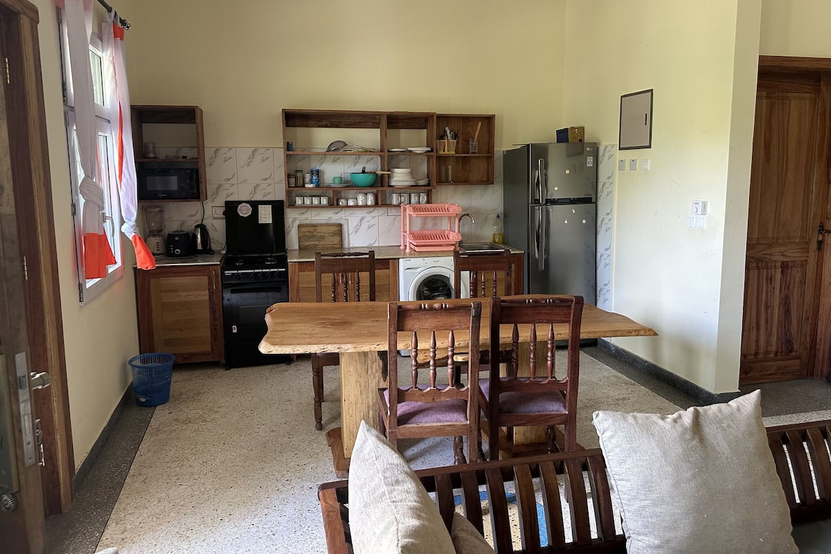 Una cocina compacta con armarios de madera, lavadora, refrigerador y un comedor con sillas y mesa de madera.