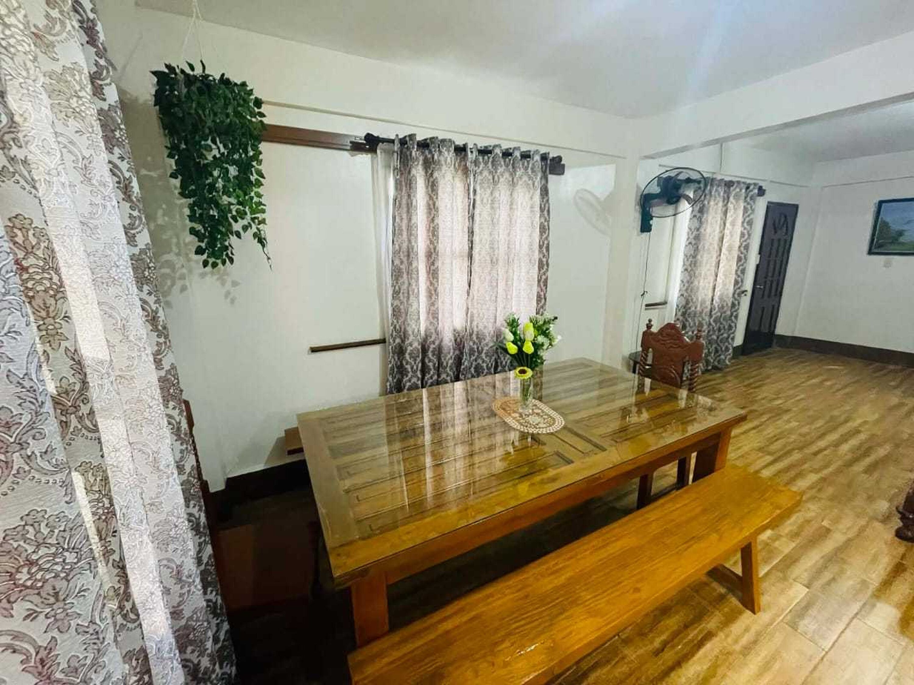 Un coin repas avec une table en bois, un banc, des rideaux à motifs et une plante suspendue.