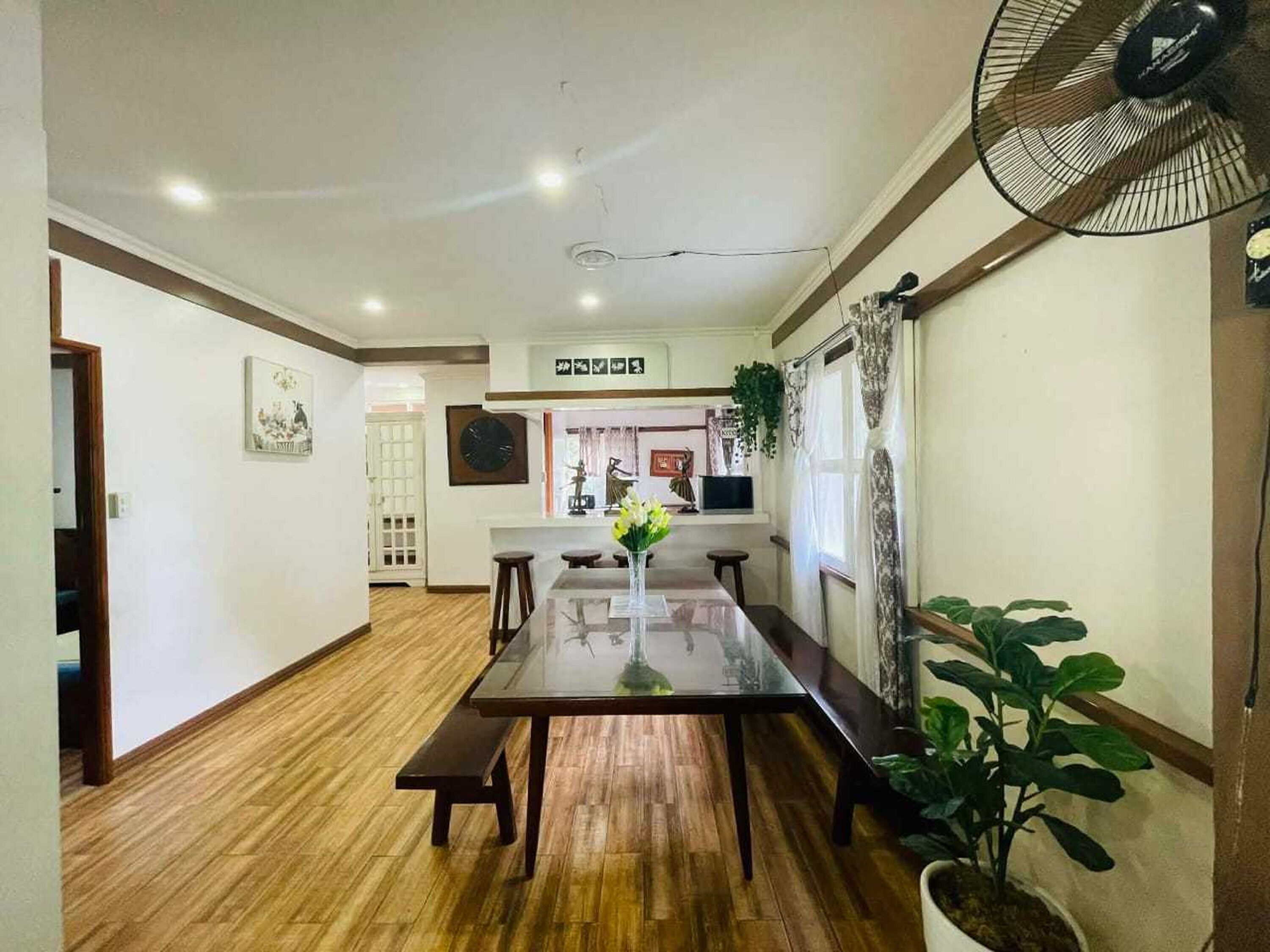 A dining area with a wooden floor, a glass-top table, and two wooden benches. There is a potted plant on the right side.