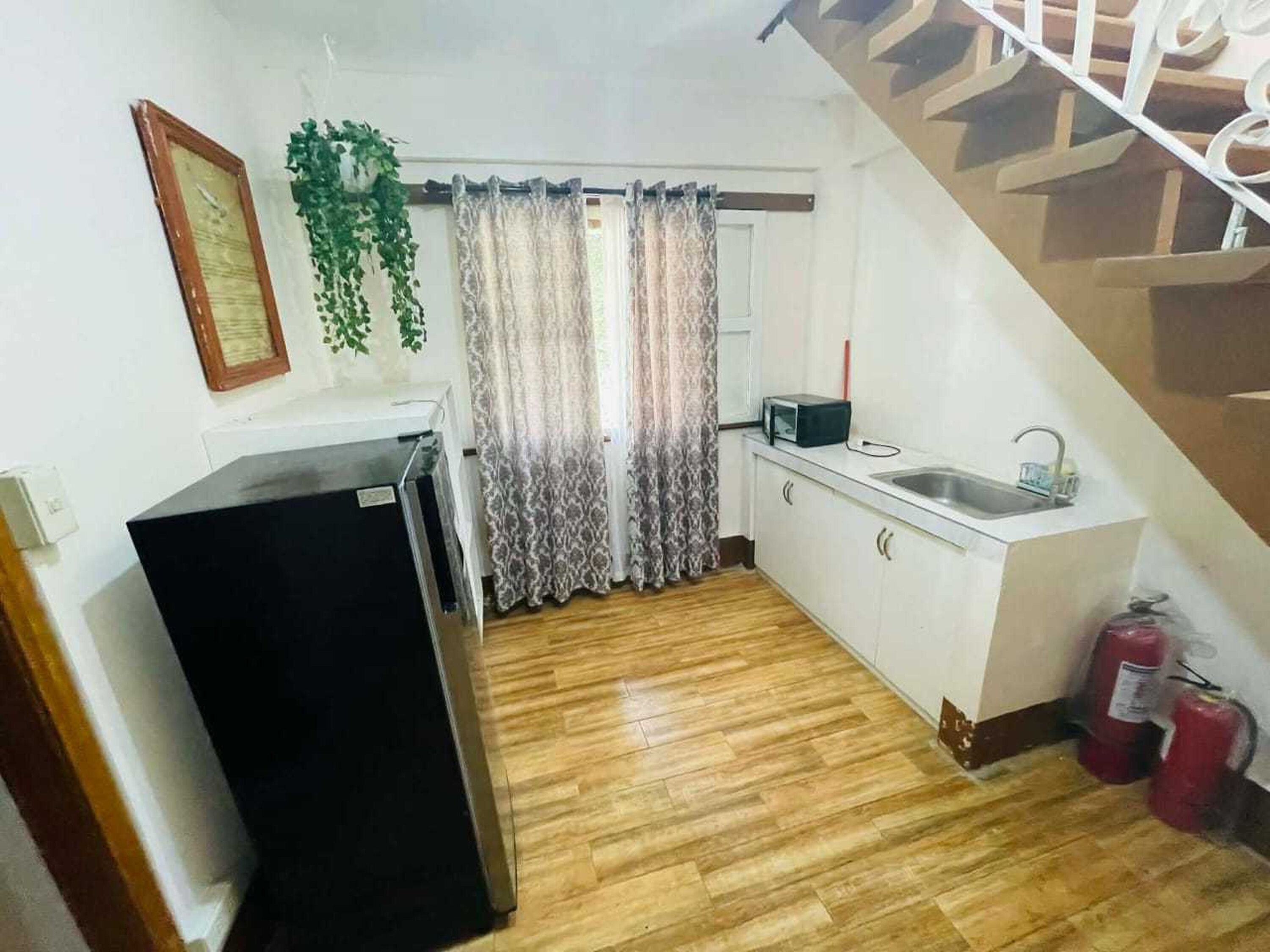 A compact kitchen with a refrigerator, microwave, sink, and fire extinguishers.