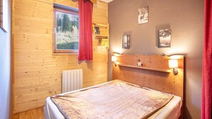 A wooden-paneled room with a bed, a window with a red curtain, and wall-mounted shelves. - Apt. in Chamrousse near supermarket (Chamrousse)