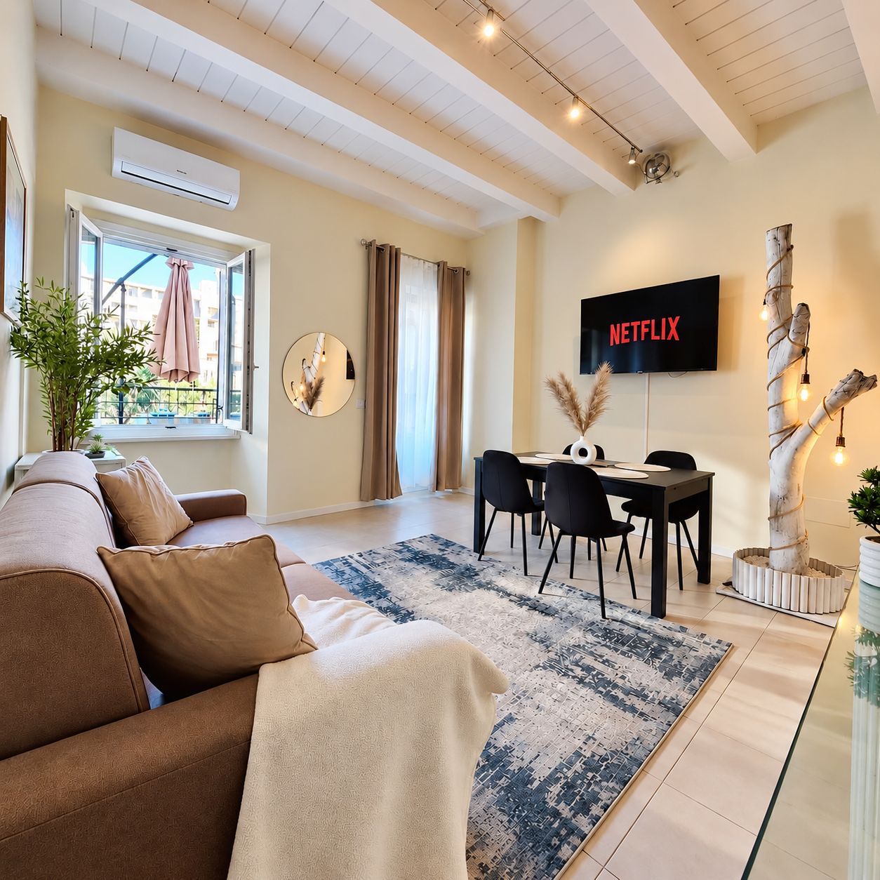 Un salon moderne comprenant un canapé, une table à manger avec des chaises, un téléviseur à écran plat et un arbre décoratif.