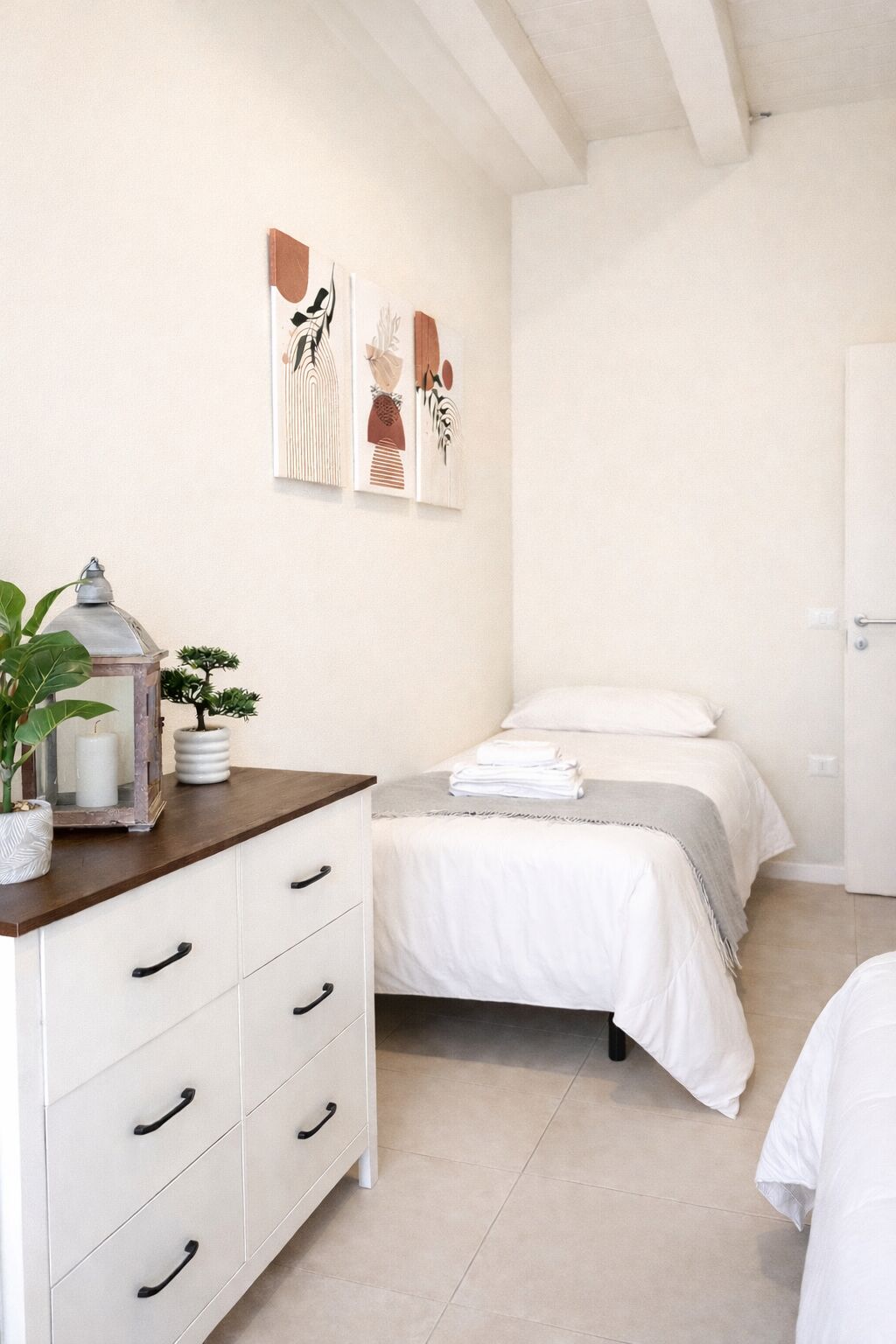 A bedroom with a bed, a dresser, a mirror, a potted plant, and wall art.