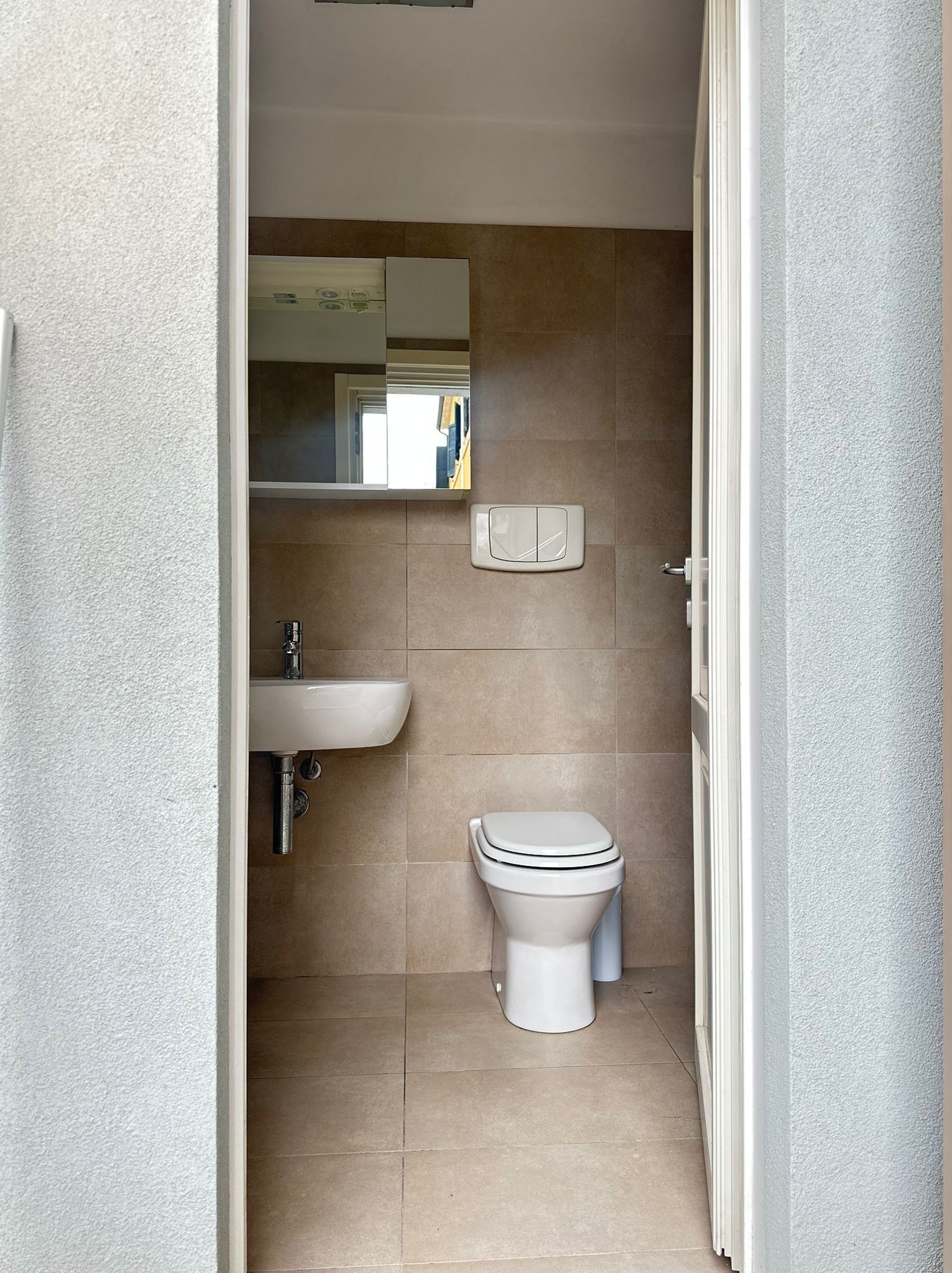 Un baño pequeño y limpio con inodoro, lavamanos y espejo.