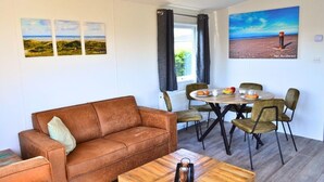 Un salon chaleureux avec un canapé en cuir marron, une table basse en bois et un coin repas comprenant une table ronde et des chaises.